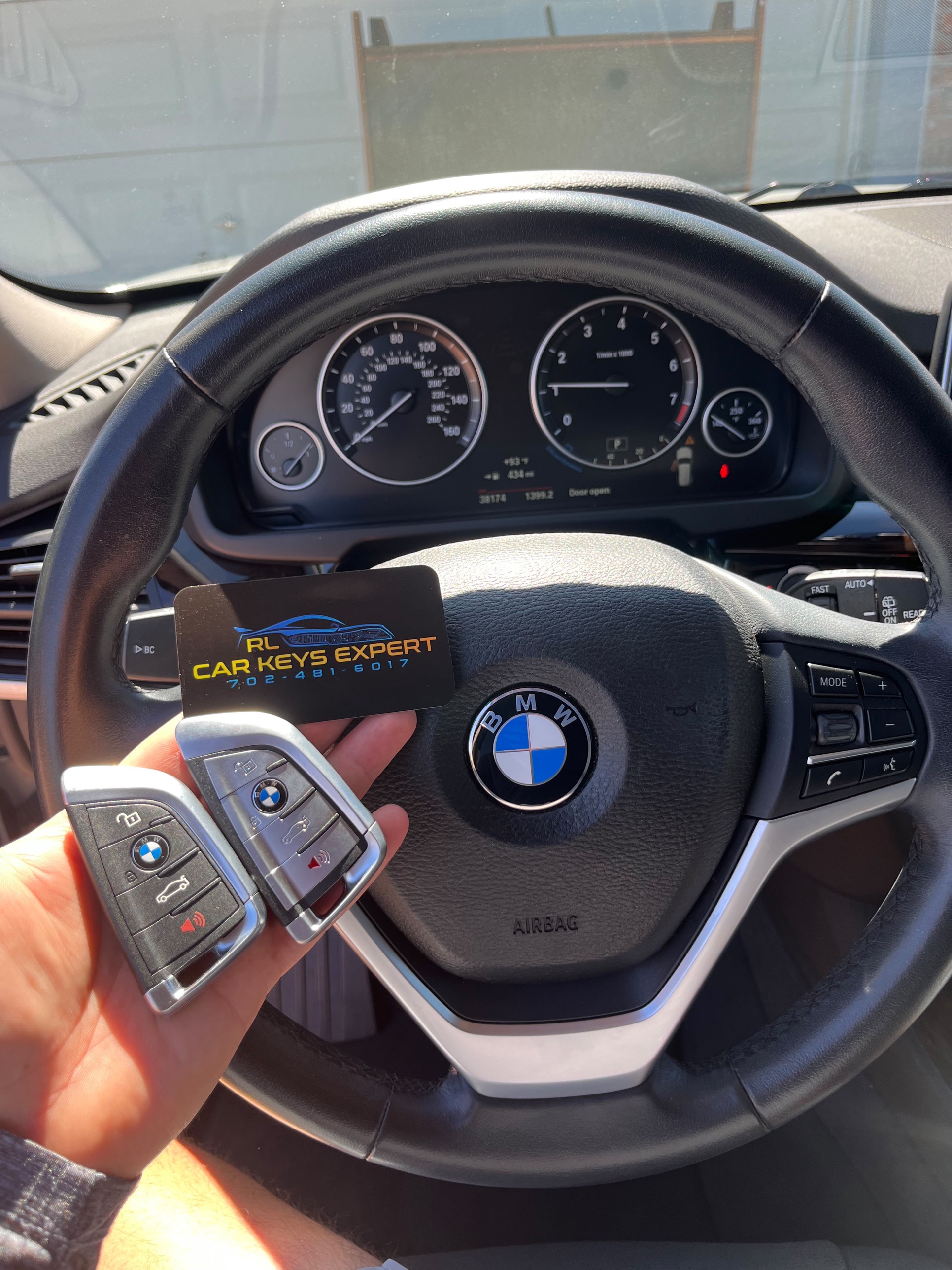 Car Keys Expert technician holding BMW keys with the steering wheel in the background